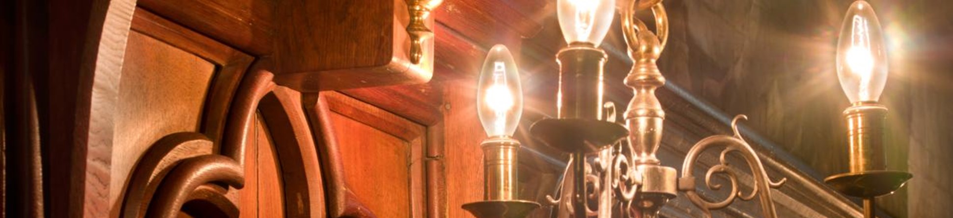 a lighting feature in a chapel. There is dark wooden paneling below the feature and a wall painting just above it