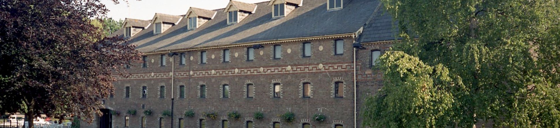 A colour photograph of the exterior of a former maltings building with a contrasting brick frieze band running above the second storey.