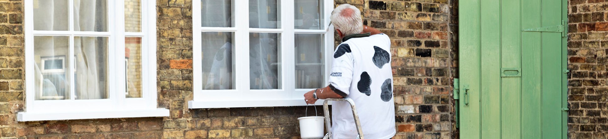 Man on step ladder painting white window frames.