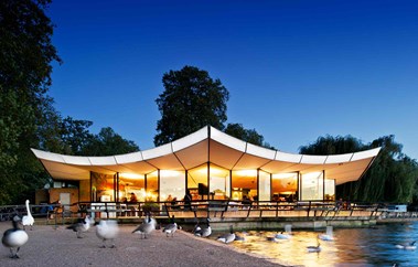 Canopied building situated next to a lake with people seated outside