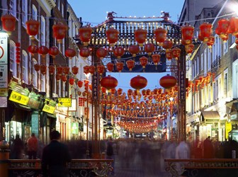 A long-exposure photograph of a street scene in London's China Town in the early evening. Red lanterns hang between buildings.